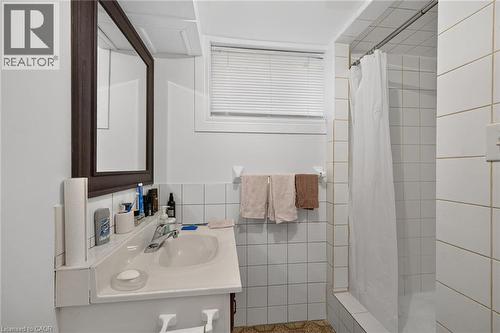 Bathroom featuring a vanity with an integrated sink, wall-mounted mirror, inset shower with white wall tiling, and a window with fitted blinds - 411 Queen Victoria Drive, Hamilton, ON 