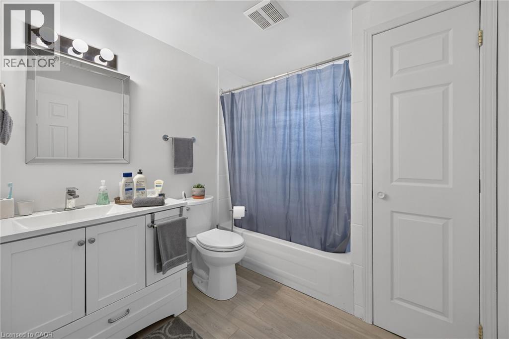 White vanity with a rectangular sink, integrated chrome faucet, framed vanity mirror with multi-bulb lighting, and wood-finish flooring - 411 Queen Victoria Drive, Hamilton, ON