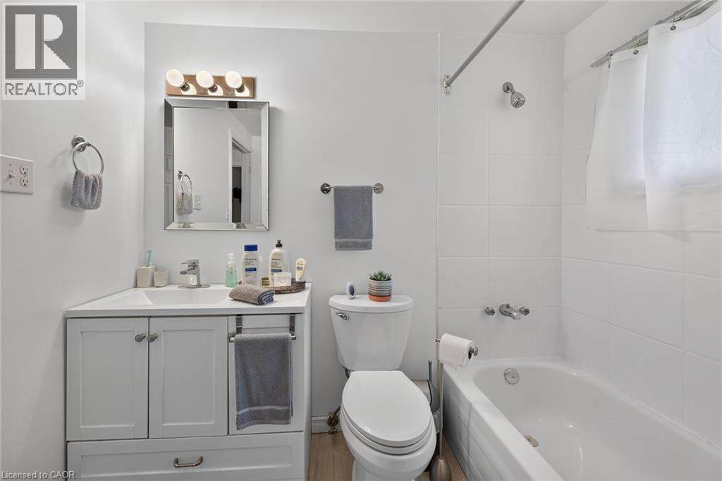 Bathroom featuring a white vanity with an integrated sink, polished chrome faucet, framed mirror, three-light fixture, and a tiled tub-shower combination - 411 Queen Victoria Drive, Hamilton, ON