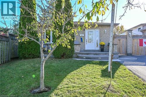 Stone veneer exterior featuring a covered front porch with recessed stair lighting, wood-finished fencing, and mature landscaping - 411 Queen Victoria Drive, Hamilton, ON 
