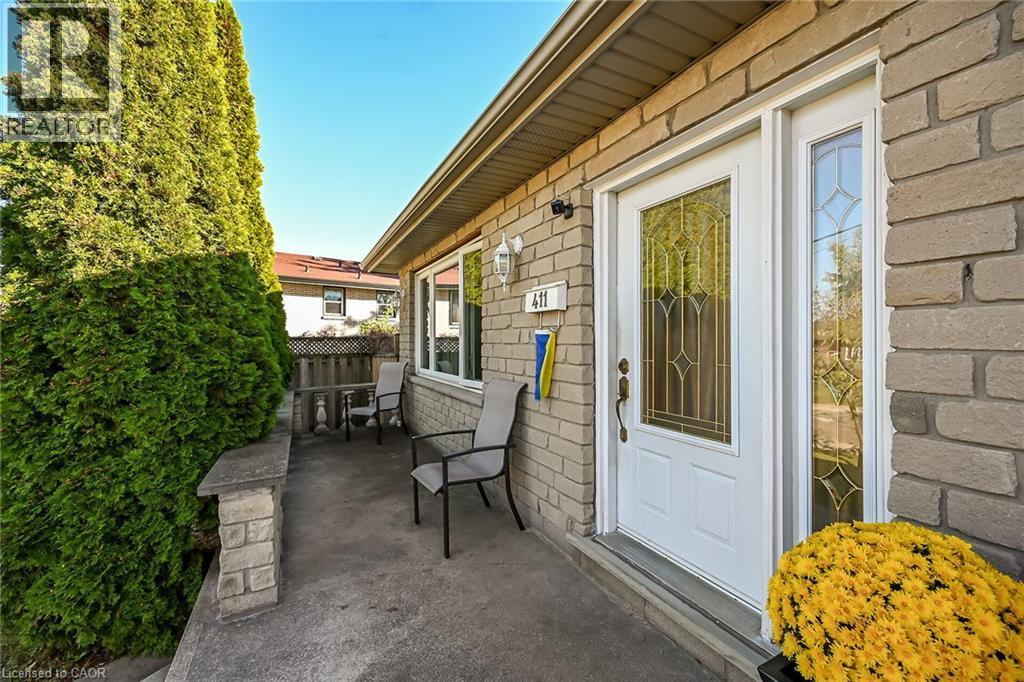 Stone masonry exterior facade with a concrete front porch, white entry door featuring decorative glass inlay, sidelight window, and wall-mounted exterior light fixture - 411 Queen Victoria Drive, Hamilton, ON