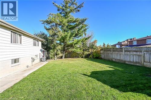 Rear yard featuring a manicured lawn, full-height perimeter wood fencing, mature evergreens, and concrete side walkway - 411 Queen Victoria Drive, Hamilton, ON 
