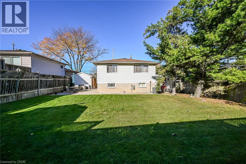 Spacious backyard featuring a manicured lawn, concrete patio, perimeter wood fencing, and mature trees - 411 Queen Victoria Drive, Hamilton, ON