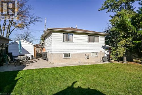 Rear exterior featuring light-colored horizontal siding, concrete masonry foundation, concrete patio, and fenced backyard with mature trees - 411 Queen Victoria Drive, Hamilton, ON 