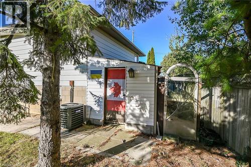 Exterior side profile featuring horizontal lap siding, a concrete masonry foundation, an attached central air conditioning unit, and an arched metal gate - 411 Queen Victoria Drive, Hamilton, ON 