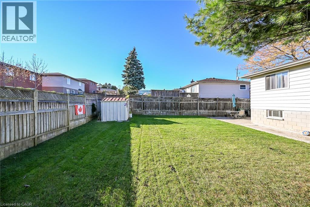 Rear yard featuring a manicured lawn, full-perimeter wood fencing, a detached storage shed, and a concrete patio area - 411 Queen Victoria Drive, Hamilton, ON