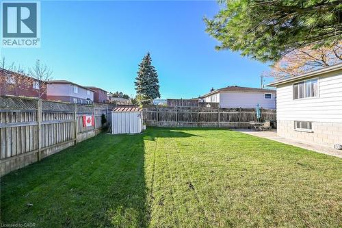 Rear yard featuring a manicured lawn, full-perimeter wood fencing, a detached storage shed, and a concrete patio area - 411 Queen Victoria Drive, Hamilton, ON 