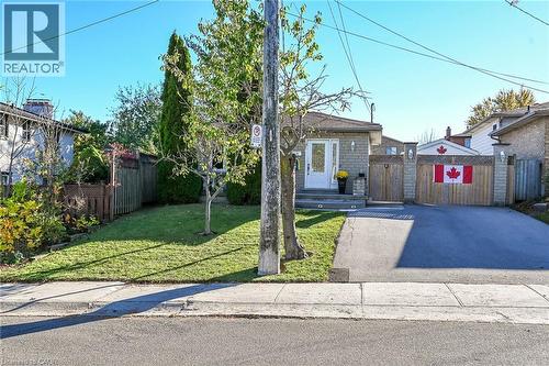 Brick exterior featuring a private asphalt driveway, integrated wood fencing, and a manicured front lawn - 411 Queen Victoria Drive, Hamilton, ON 