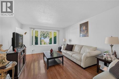 Living area featuring wood-finish flooring, white walls, and a multi-pane window with vertical blinds - 411 Queen Victoria Drive, Hamilton, ON 