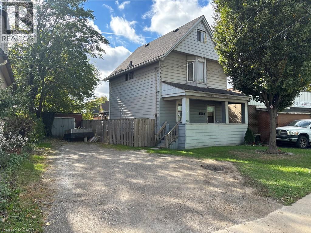 Two-story residence featuring horizontal siding, a covered front porch, a gravel driveway, and a wooden privacy fence - 372 Beach Road, Hamilton, ON