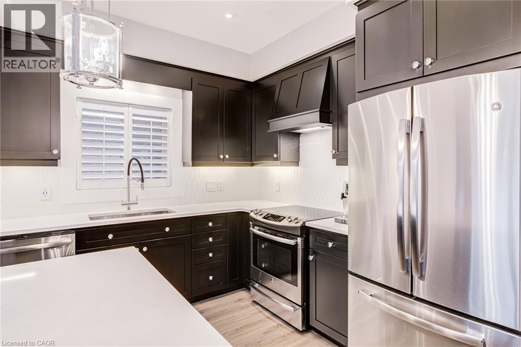 Kitchen featuring stainless steel appliances, hanging light fixtures, light wood-style floors, and light stone counters - 239 Cranbrook Street, Kitchener, ON - Indoor Photo Showing Kitchen