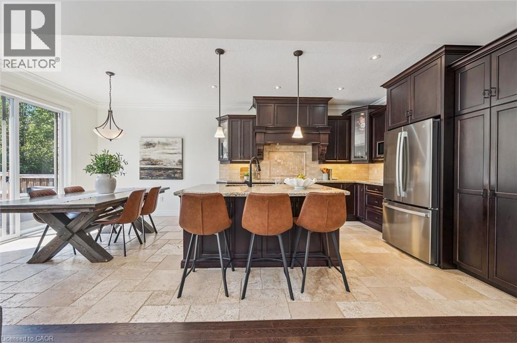 Open-concept kitchen and dining area featuring dark wood cabinetry, stainless steel appliances, a center island with countertop seating, and stone tile flooring. - 828 Copper Ridge Drive, Waterloo, ON - Indoor
