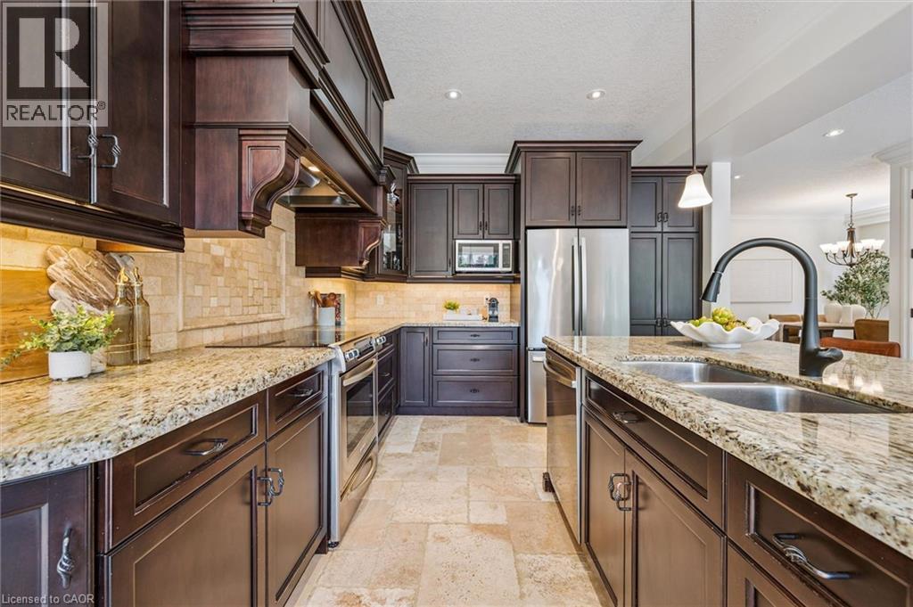 Gourmet kitchen featuring rich wood cabinetry, stainless steel appliances, stone slab countertops, a tile backsplash, and recessed lighting - 828 Copper Ridge Drive, Waterloo, ON - Indoor Photo Showing Kitchen With Double Sink With Upgraded Kitchen