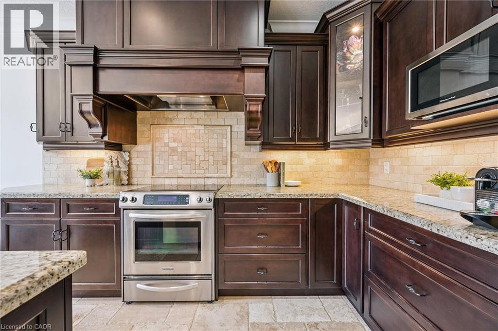 Kitchen featuring rich wood cabinetry, stone countertops, a tile backsplash, and stainless steel appliances including a range and microwave. - 828 Copper Ridge Drive, Waterloo, ON - Indoor Photo Showing Kitchen With Upgraded Kitchen