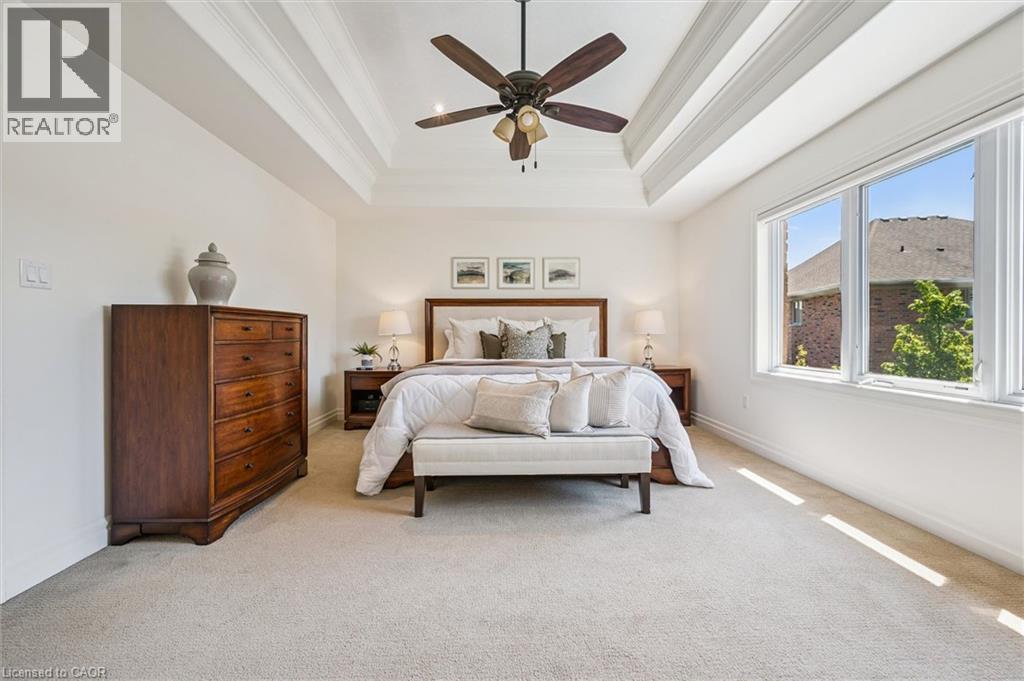 Spacious primary featuring a tray ceiling with a ceiling fan, light-toned carpeting, and a large multi-pane window. - 828 Copper Ridge Drive, Waterloo, ON - Indoor Photo Showing Bedroom
