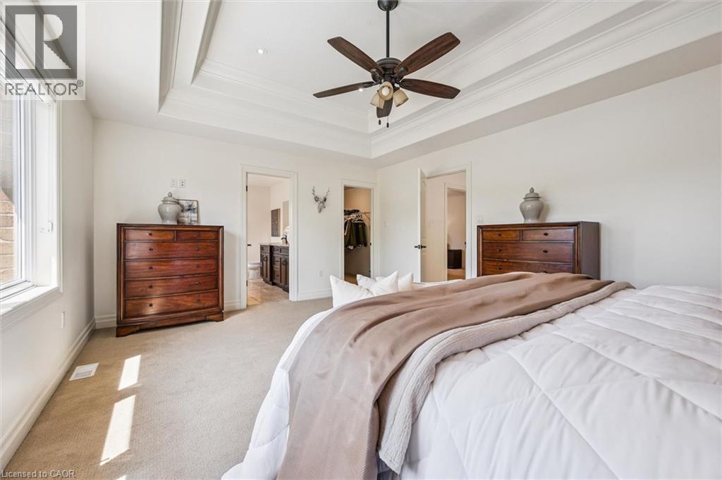 Primary Bedroom featuring a tray ceiling with crown molding, ceiling fan with integrated lighting, broad window, and carpet flooring. - 828 Copper Ridge Drive, Waterloo, ON - Indoor Photo Showing Bedroom