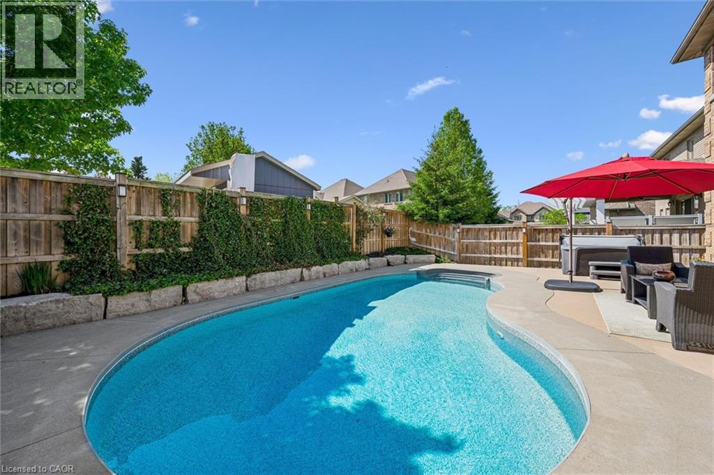 Curved inground pool with surrounding concrete patio. - 828 Copper Ridge Drive, Waterloo, ON - Outdoor With In Ground Pool With Backyard
