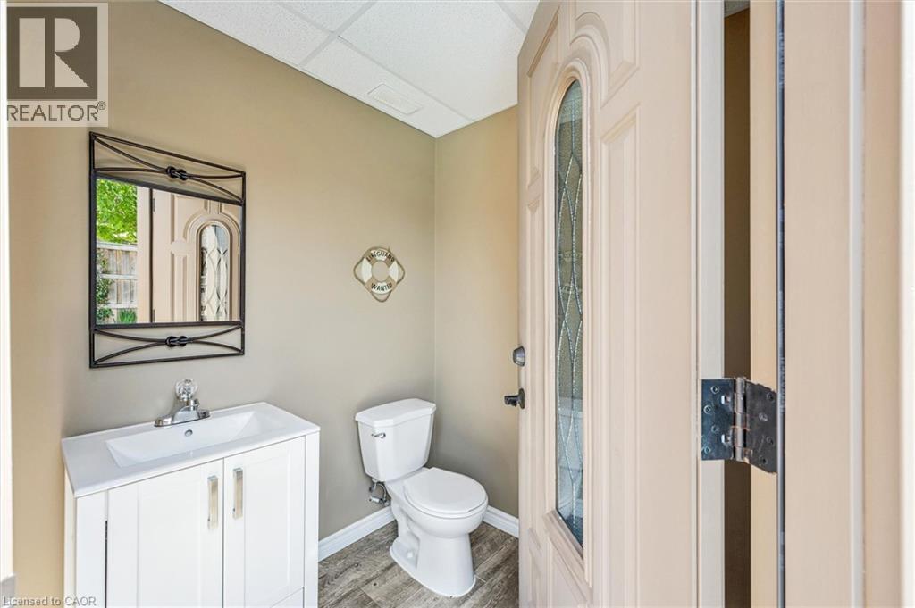 Outdoor powder room featuring a white single-sink vanity, coordinating toilet, and wood-finish flooring. - 828 Copper Ridge Drive, Waterloo, ON - Indoor Photo Showing Bathroom