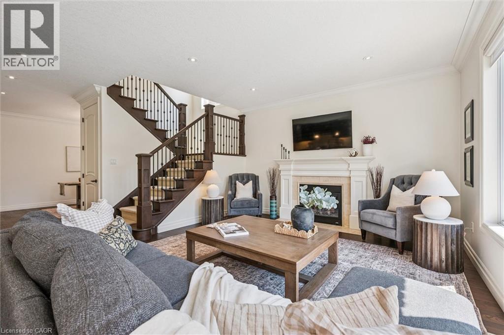 Living space featuring a stone-clad fireplace with a decorative mantle, recessed lighting, crown molding, a dark wood-finish staircase with wrought iron spindles, and wood-finish flooring. - 828 Copper Ridge Drive, Waterloo, ON - Indoor Photo Showing Living Room With Fireplace