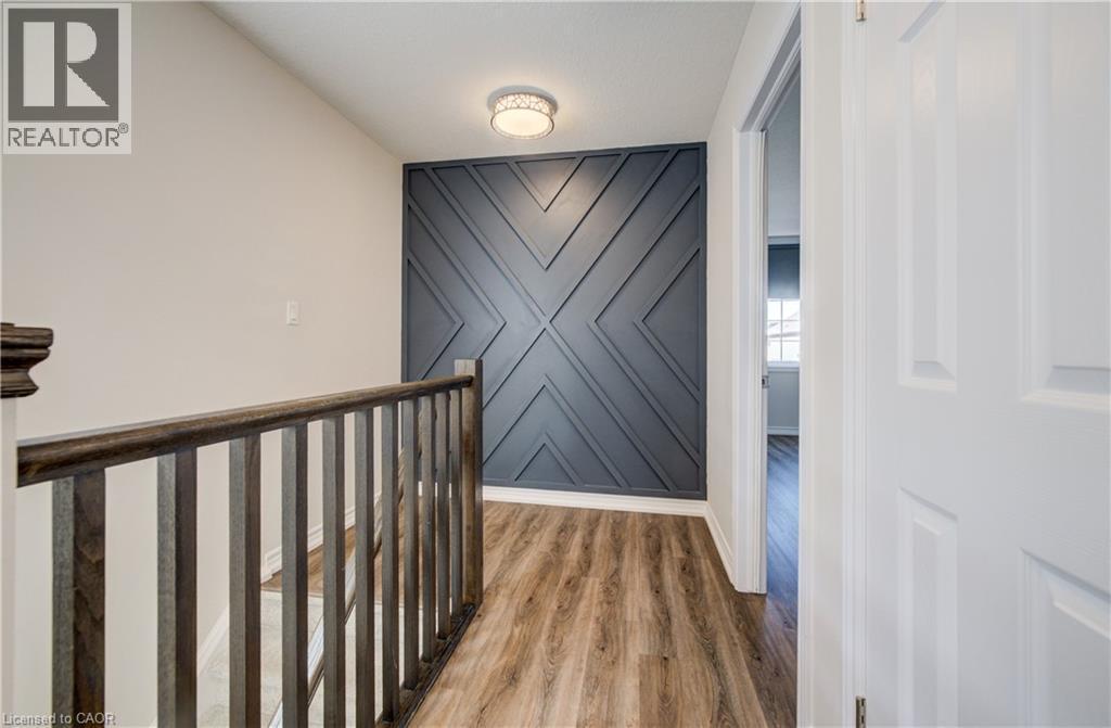 Upper-level hallway featuring wood-finish flooring, a decorative accent wall with geometric paneling, and a contemporary flush-mount ceiling light - 80 Miranda Path, Elmira, ON - Indoor Photo Showing Other Room