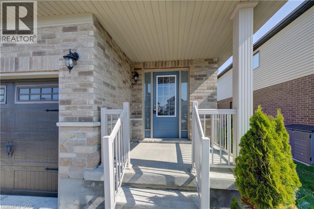 Brick and stone facade featuring a covered front porch with white railings, a blue entry door with a sidelight, and a decorative outdoor light fixture - 80 Miranda Path, Elmira, ON - Outdoor With Exterior