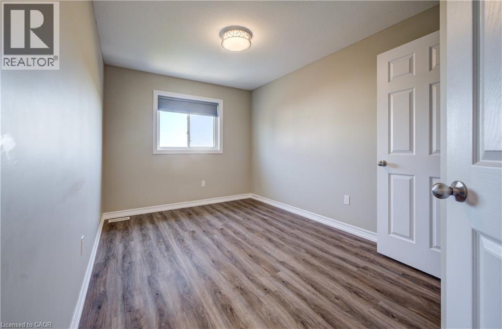 Wood-finish flooring throughout, featuring a window with a roller shade, a ceiling-mounted light fixture, and white painted trim - 80 Miranda Path, Elmira, ON - Indoor Photo Showing Other Room