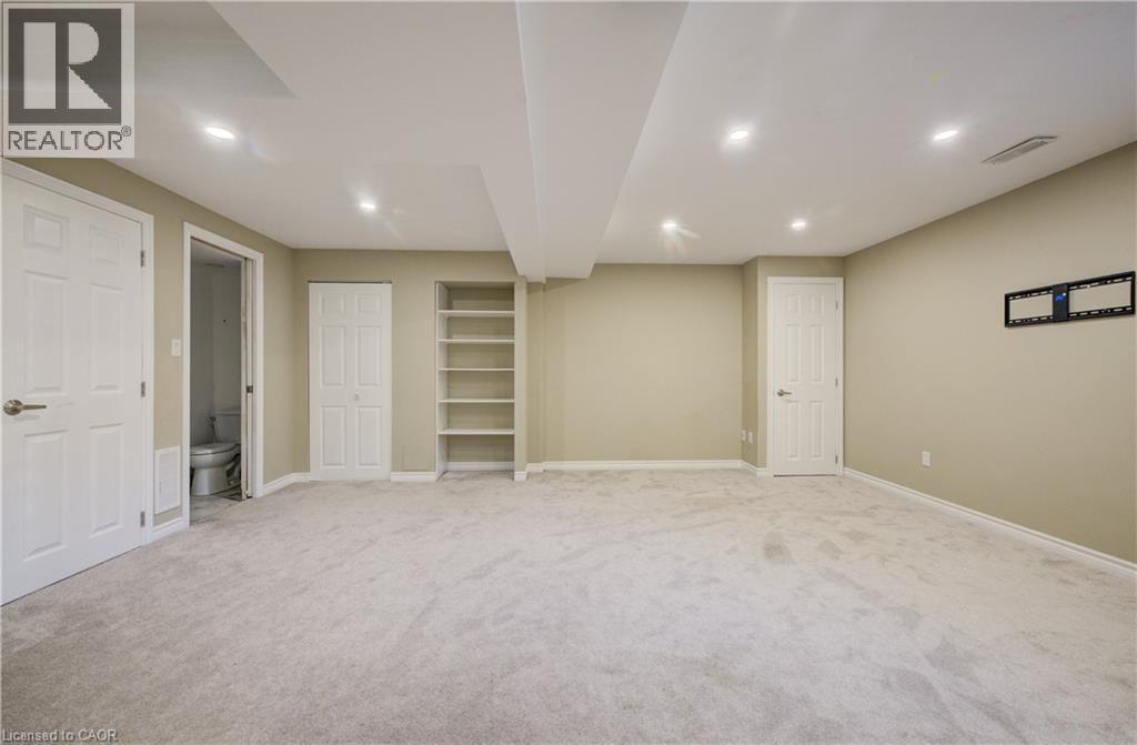 Spacious room featuring light-colored carpet, recessed ceiling lighting, built-in shelving, and multiple white panel doors - 80 Miranda Path, Elmira, ON - Indoor Photo Showing Basement