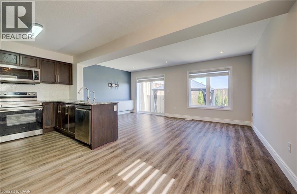 Open-concept living area featuring wood-finish flooring, a kitchen island with a sink and stainless steel appliances, recessed lighting, and sliding glass doors to the exterior - 80 Miranda Path, Elmira, ON - Indoor Photo Showing Kitchen