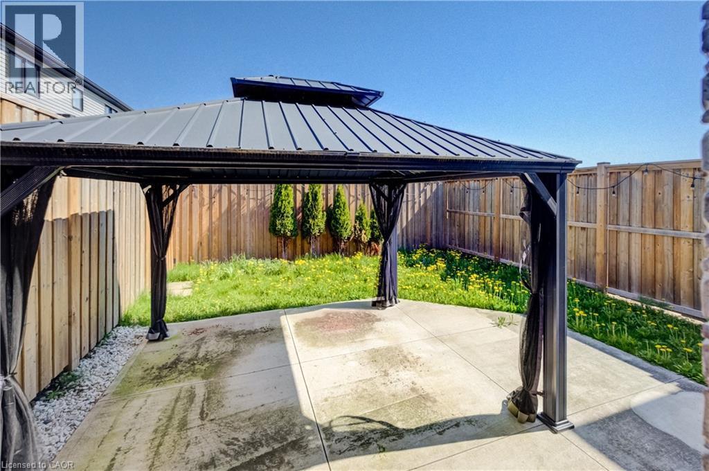 Backyard gazebo with a metal roof and privacy screens, featuring a concrete patio, a green lawn, and wood fencing - 80 Miranda Path, Elmira, ON - Outdoor