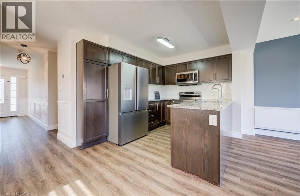 Kitchen featuring wood-finish flooring, dark wood cabinetry, stainless steel appliances, and a central island with a granite countertop and undermount sink - 80 Miranda Path, Elmira, ON - Indoor Photo Showing Kitchen With Upgraded Kitchen