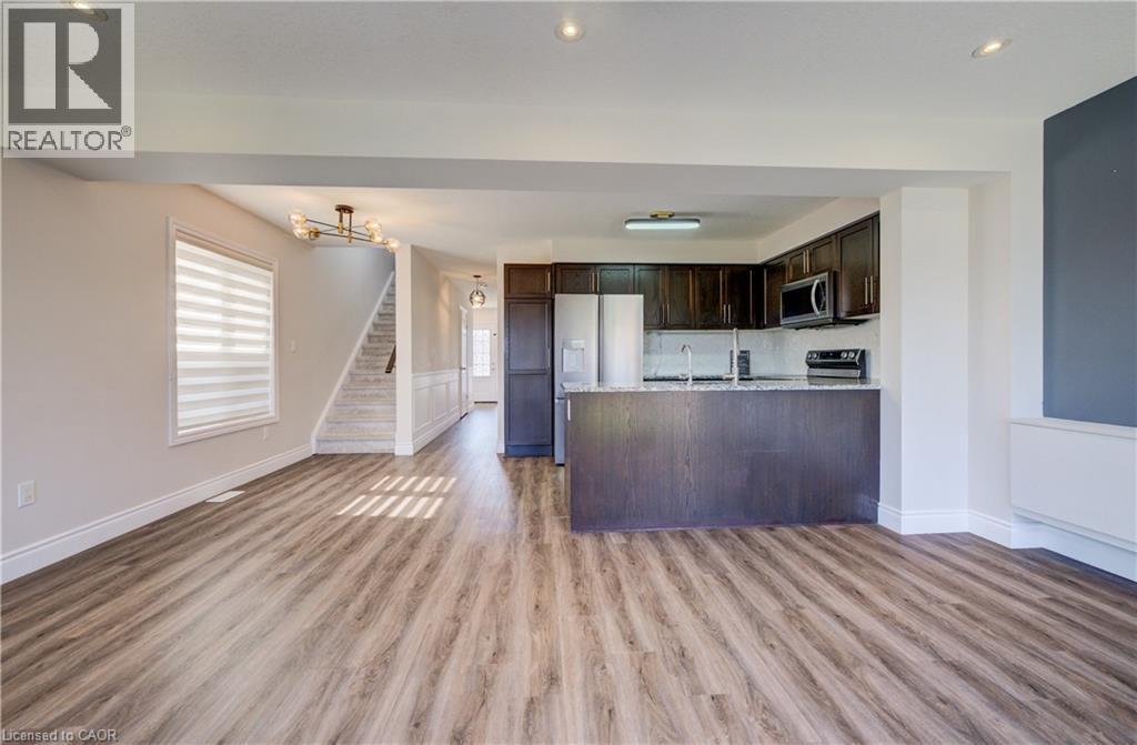 Open-concept living space featuring wood-finish flooring, a contemporary kitchen with dark cabinetry, stainless steel appliances, a breakfast bar, and recessed lighting - 80 Miranda Path, Elmira, ON - Indoor Photo Showing Kitchen