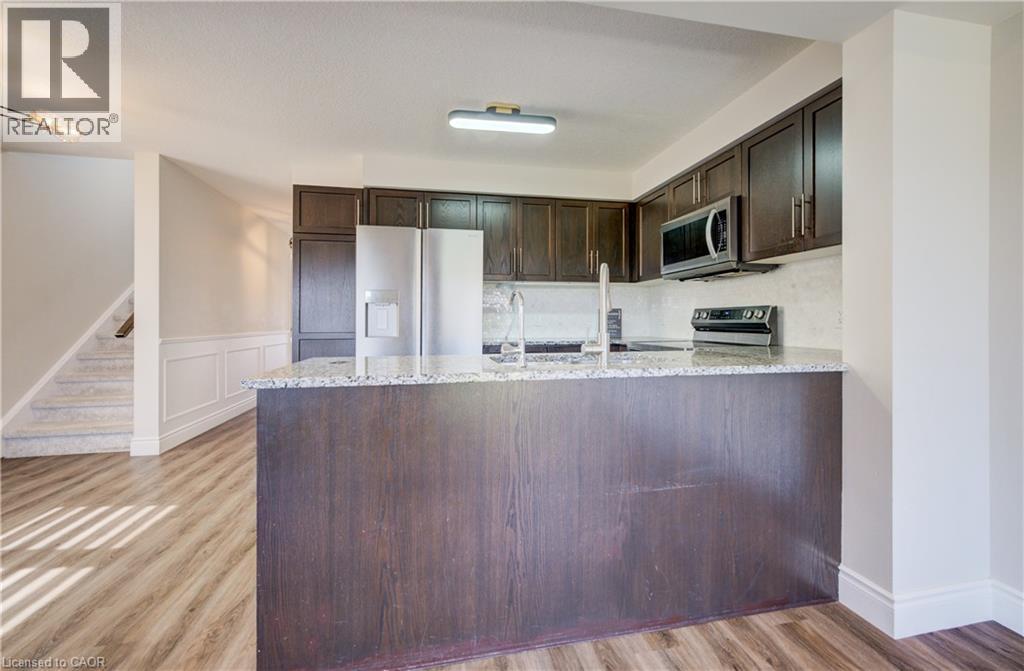 Kitchen featuring dark wood cabinetry, stainless steel appliances, a stone-finish countertop, and a tile-finish backsplash - 80 Miranda Path, Elmira, ON - Indoor Photo Showing Kitchen