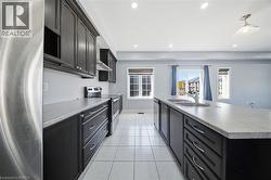Modern kitchen featuring dark cabinetry, stainless steel appliances, a center island with double sink, light-toned countertops, and recessed lighting - 