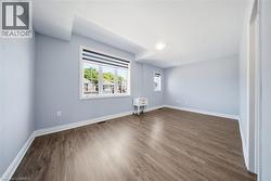 Expansive room featuring wood-finish flooring, light blue walls, white trim, and a prominent multi-pane window with a roller shade - 