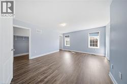 Spacious room featuring wood-finish flooring, light blue walls, white trim, and two windows with blinds - 