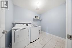 Functional utility room featuring white tile flooring, light blue wall paint, and white baseboards - 