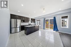 Open-concept kitchen and living area featuring dark wood-finish cabinetry, stainless steel appliances, a kitchen island with a stone-finish countertop, and tile flooring - 