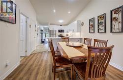 Open-concept dining area featuring wood-finish flooring, recessed lighting, and a kitchen with white cabinetry and stainless steel appliances - 