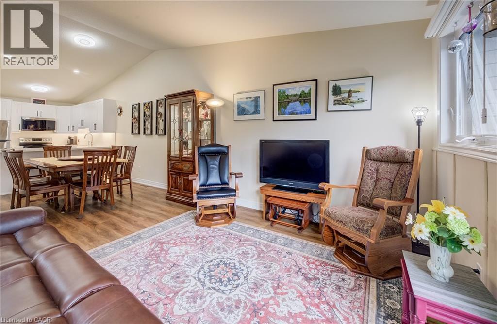 Vaulted ceiling with recessed lighting, wood-finish flooring, white kitchen cabinetry, stainless steel appliances, and a built-in window with paneling - 16 Steed Court, Brantford, ON