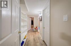 Bright hallway featuring wood-finish flooring, multiple white panel doors with brass hardware, and abundant natural lighting from recessed ceiling fixtures - 