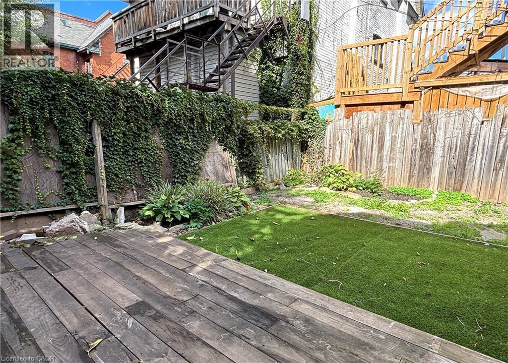 Backyard shared space featuring a wood-finish deck and green artificial turf - 76 Wentworth Street S, Hamilton, ON