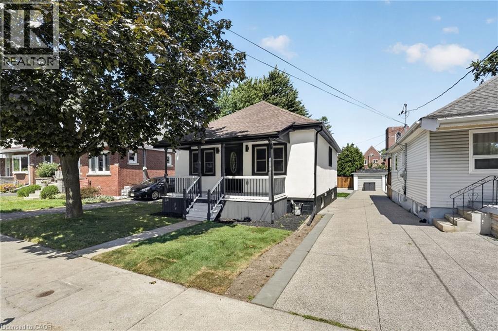 White exterior with black trim, covered front porch, concrete driveway, and detached garage - 43 E Brucedale Avenue E, Hamilton, ON