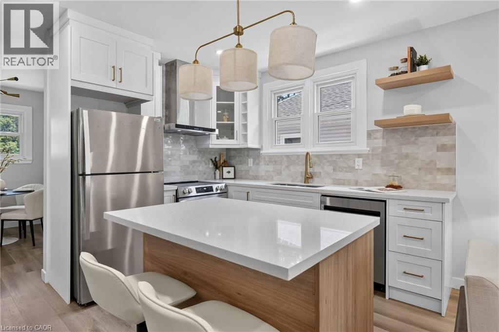 Kitchen featuring wood-finish flooring, white cabinetry with gold-tone hardware, stainless steel appliances, a center island with a white countertop, and a tiled backsplash - 43 E Brucedale Avenue E, Hamilton, ON