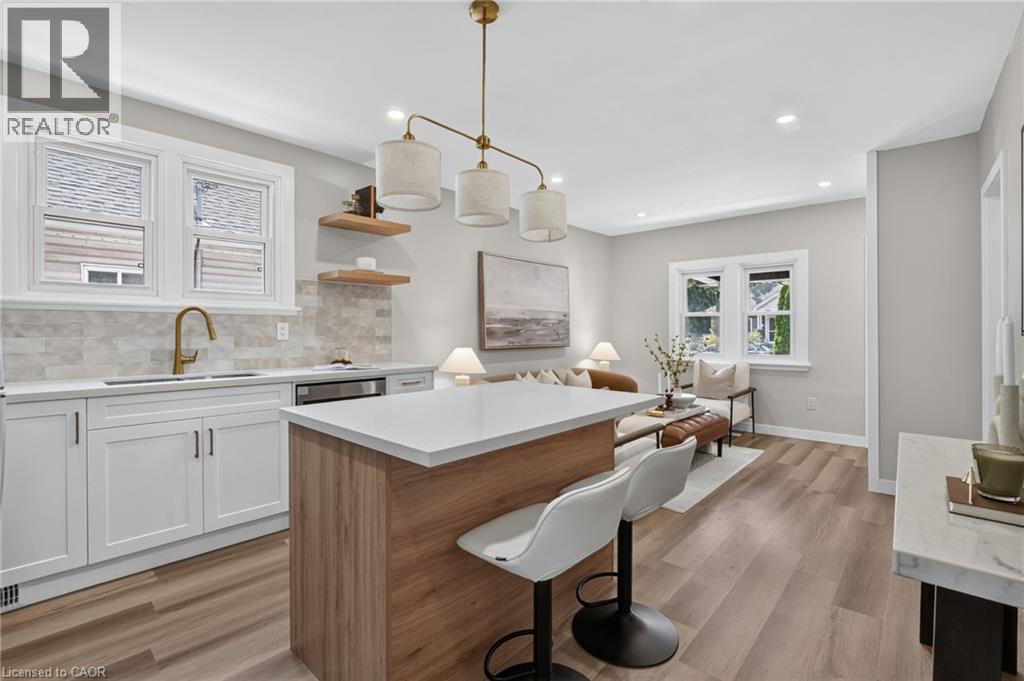 Kitchen island with a light wood finish and white countertop, white cabinetry with dark hardware, gold-toned faucet, and light wood-finish flooring - 43 E Brucedale Avenue E, Hamilton, ON