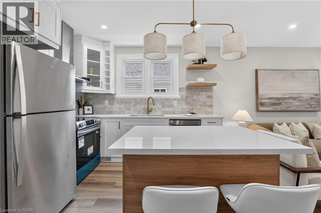 Contemporary kitchen featuring light wood-finish flooring, white cabinetry, a large center island with a white countertop, and a tiled backsplash - 43 E Brucedale Avenue E, Hamilton, ON