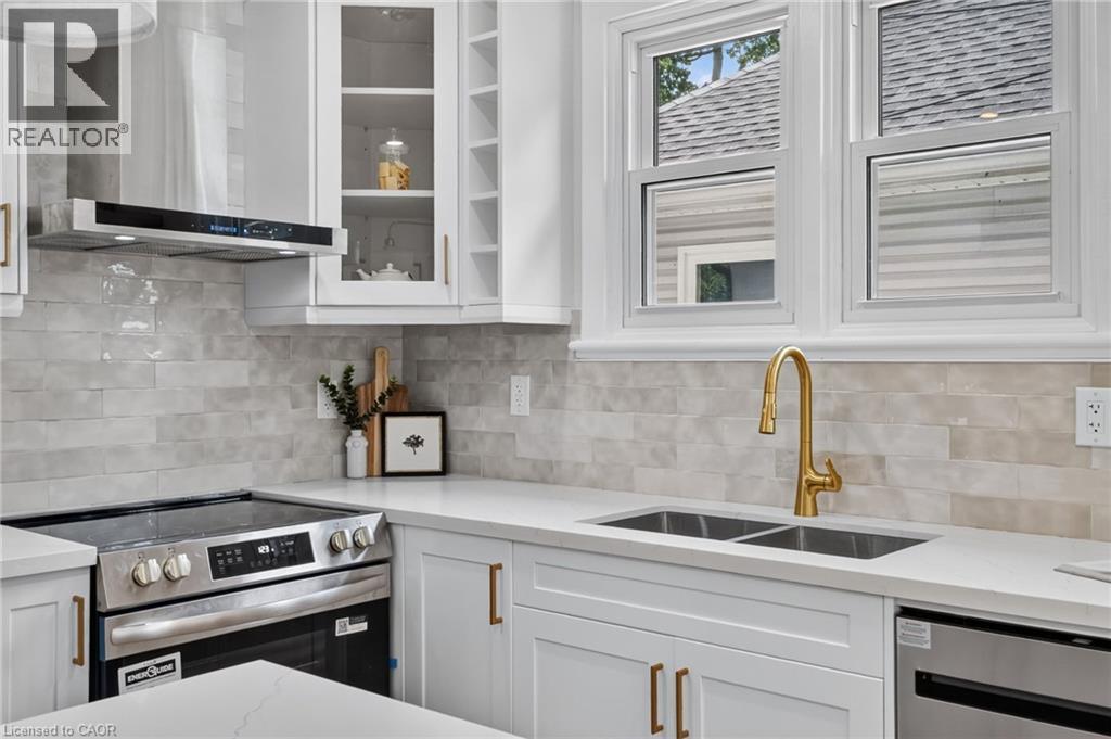 Modern kitchen featuring white cabinetry with brass-finish hardware, stainless steel appliances, and a double-basin sink with a brass-finish faucet - 43 E Brucedale Avenue E, Hamilton, ON