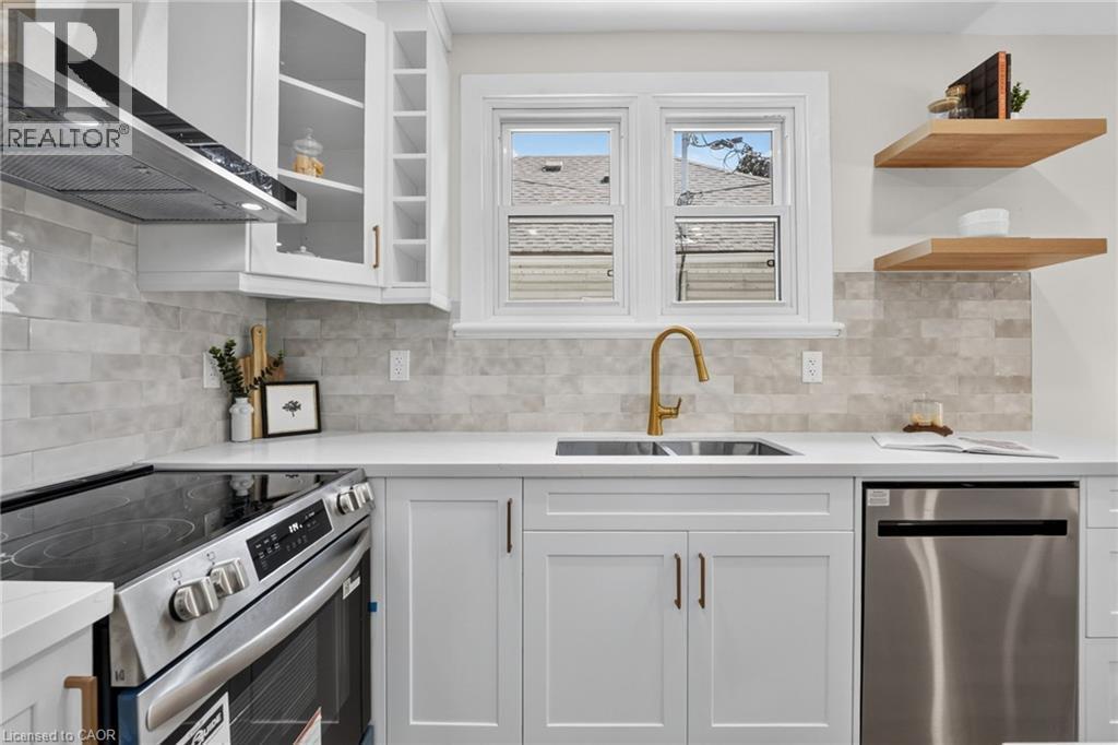 White shaker cabinetry with gold-tone hardware, stainless steel appliances, light-toned stone-finish backsplash, white quartz countertops, and a gold-tone faucet - 43 E Brucedale Avenue E, Hamilton, ON