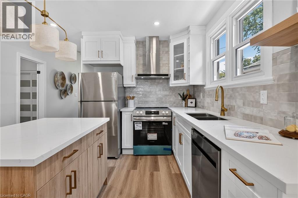 Modern kitchen with white cabinetry, stainless steel appliances, wood-finish flooring, and a stone-look backsplash - 43 E Brucedale Avenue E, Hamilton, ON