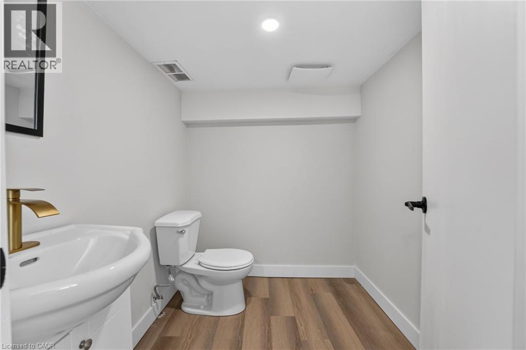 Wood-finish flooring, modern pedestal sink, gold-finish faucet, and recessed lighting - 43 E Brucedale Avenue E, Hamilton, ON