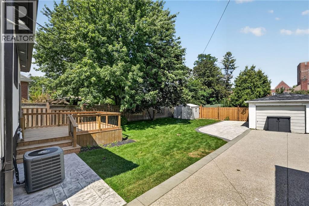 Expansive backyard featuring a multi-level wood deck, manicured lawn, concrete patio, and detached garage - 43 E Brucedale Avenue E, Hamilton, ON